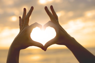 Hands showing heart for the sun on the beach.